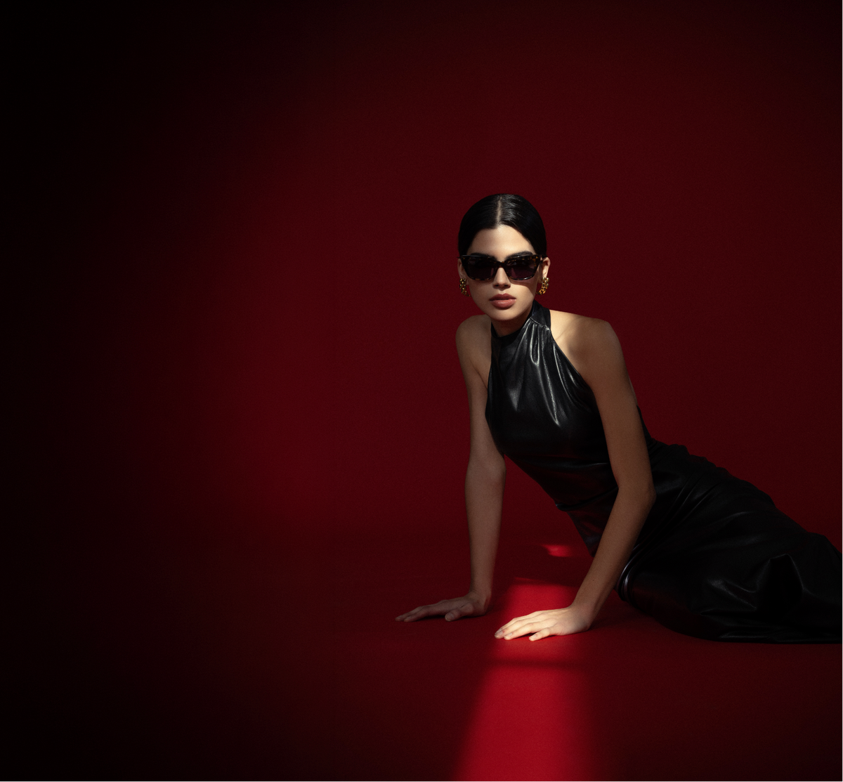 Woman in a black dress and sunglasses on a red background